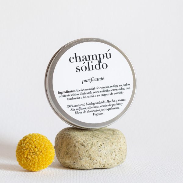 Champú Sólido Purificante debajo de una caja metálica que muestra los ingredientes del producto y al lado de un madroño amarillo.