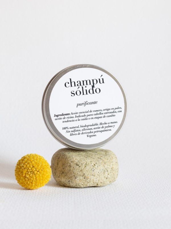 Champú Sólido Purificante debajo de una caja metálica que muestra los ingredientes del producto y al lado de un madroño amarillo.